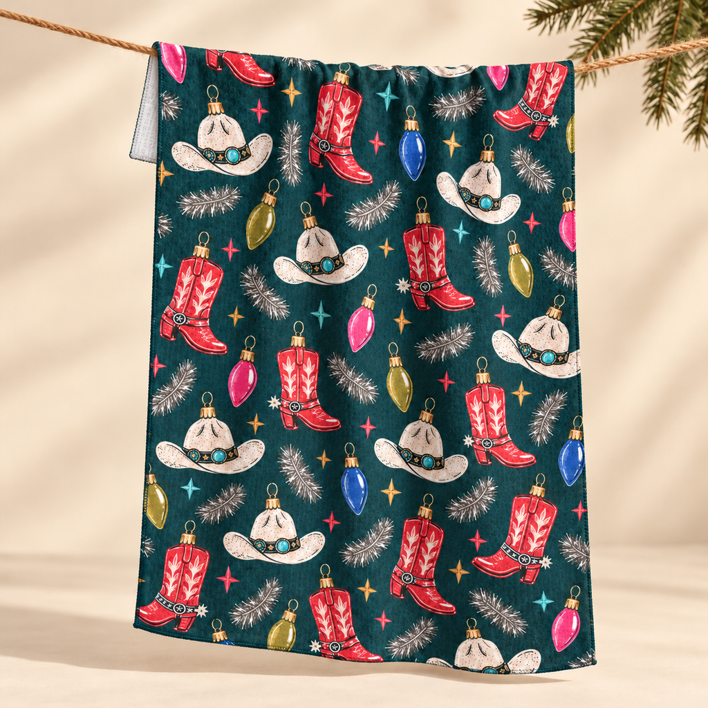 Cowboy Christmas tea towel with boots, hats and ornaments on deep teal, hanging from a line