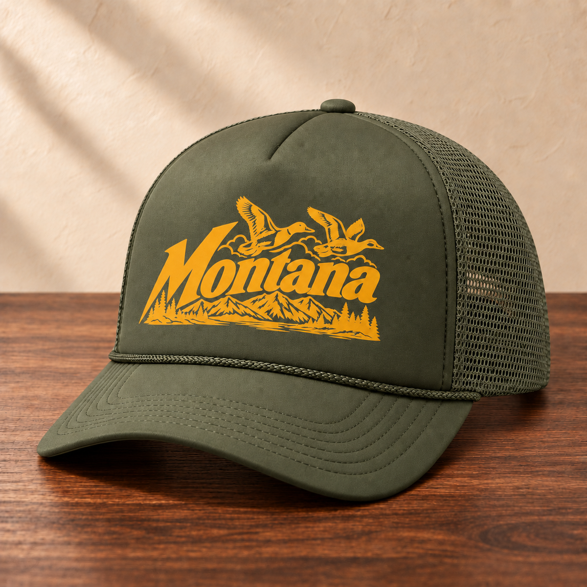 Olive Montana ducks hat with golden orange artwork and matching olive mesh, angled view on dark wood against a cream studio wall