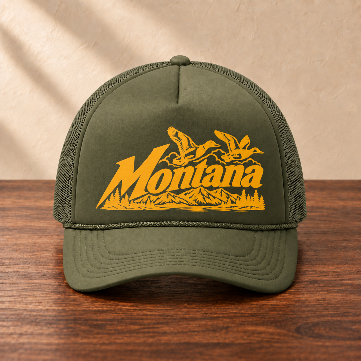 Olive Montana ducks hat with golden orange artwork and matching olive mesh, front view on dark wood against a cream studio wall