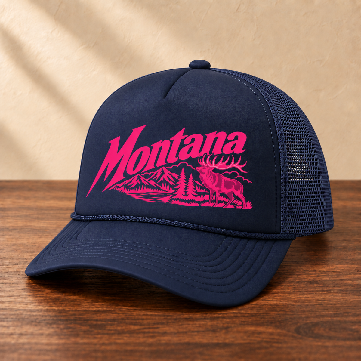 Navy Montana elk hat with hot pink artwork and matching navy mesh, angled view on dark wood against a cream studio wall