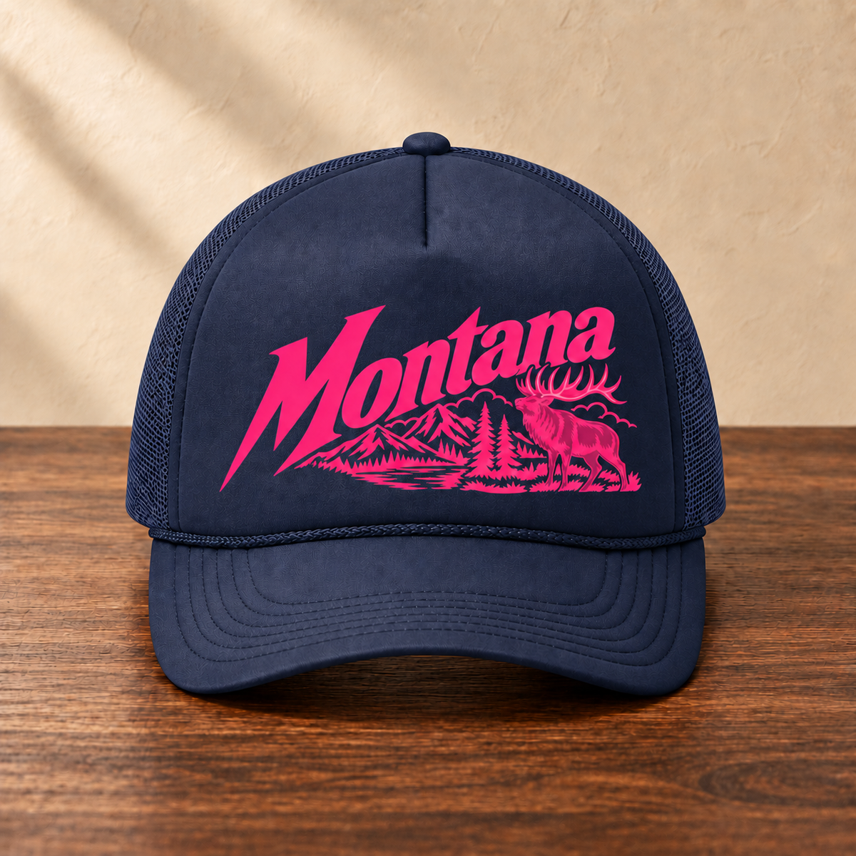 Navy Montana elk hat with hot pink artwork and matching navy mesh, front view on dark wood against a cream studio wall
