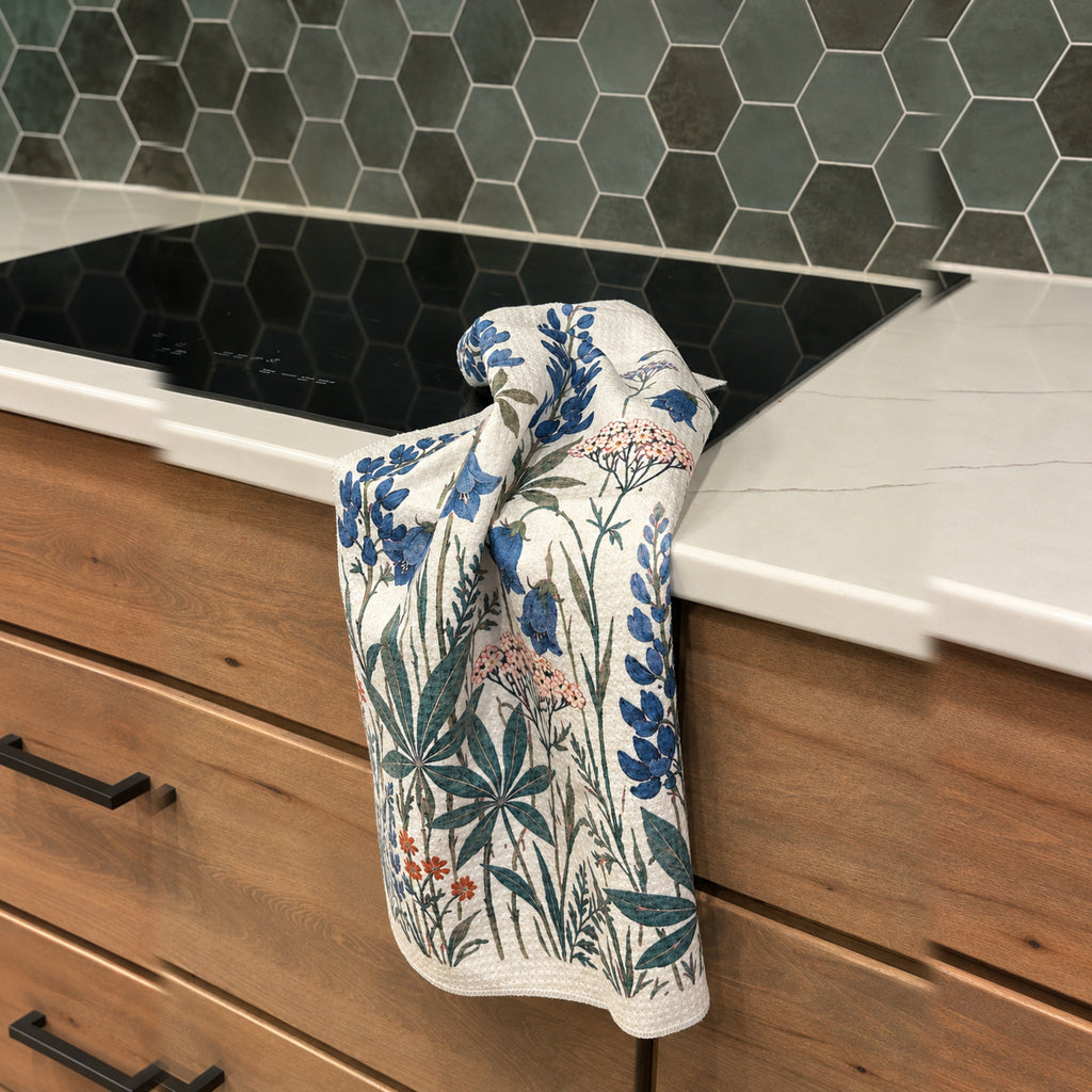 Lupine and bellflower kitchen towel draped beside a black sink and wood cabinets
